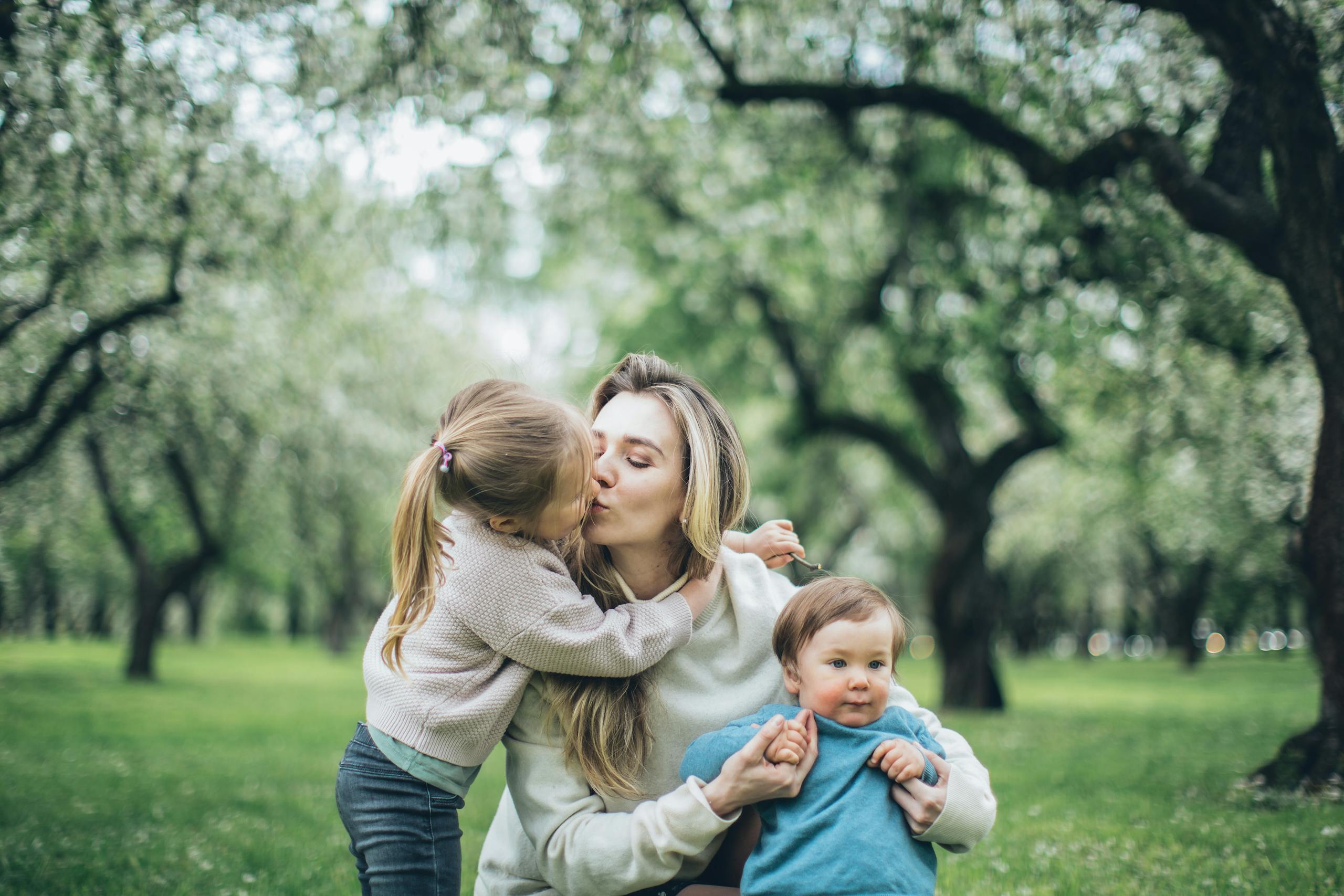 A warm family moment as a mother holds her children in a blooming spring park.