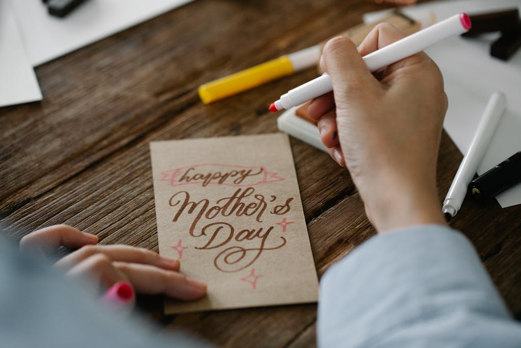 Close-up of a person designing a Mother's Day card with calligraphy on wooden table, showcasing non-toxic Mother's day gifts.