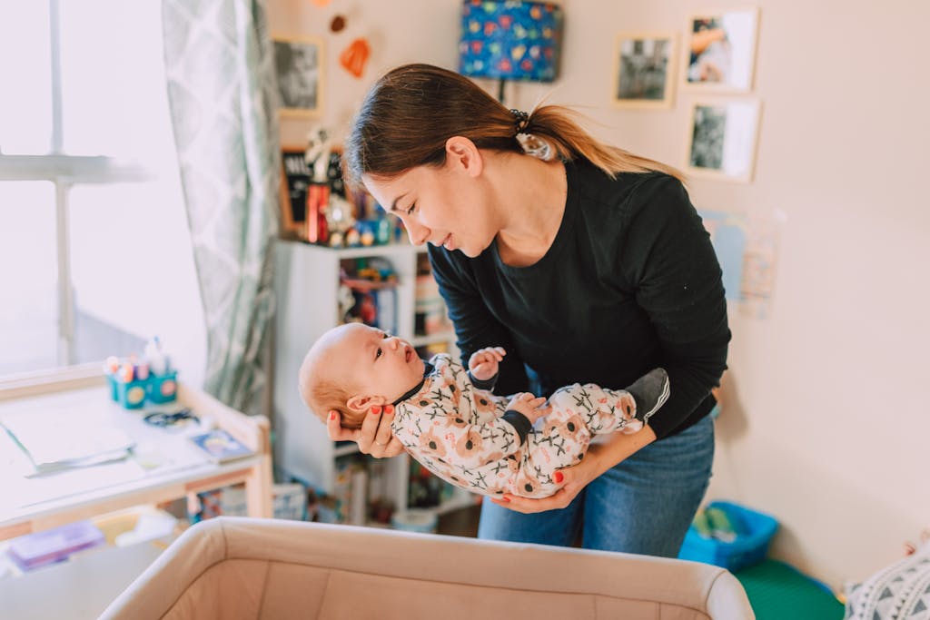 Mother lovingly holds newborn above a bassinet in a cozy nursery, reinforcing non-toxic bassinet and safe-sleep themes
