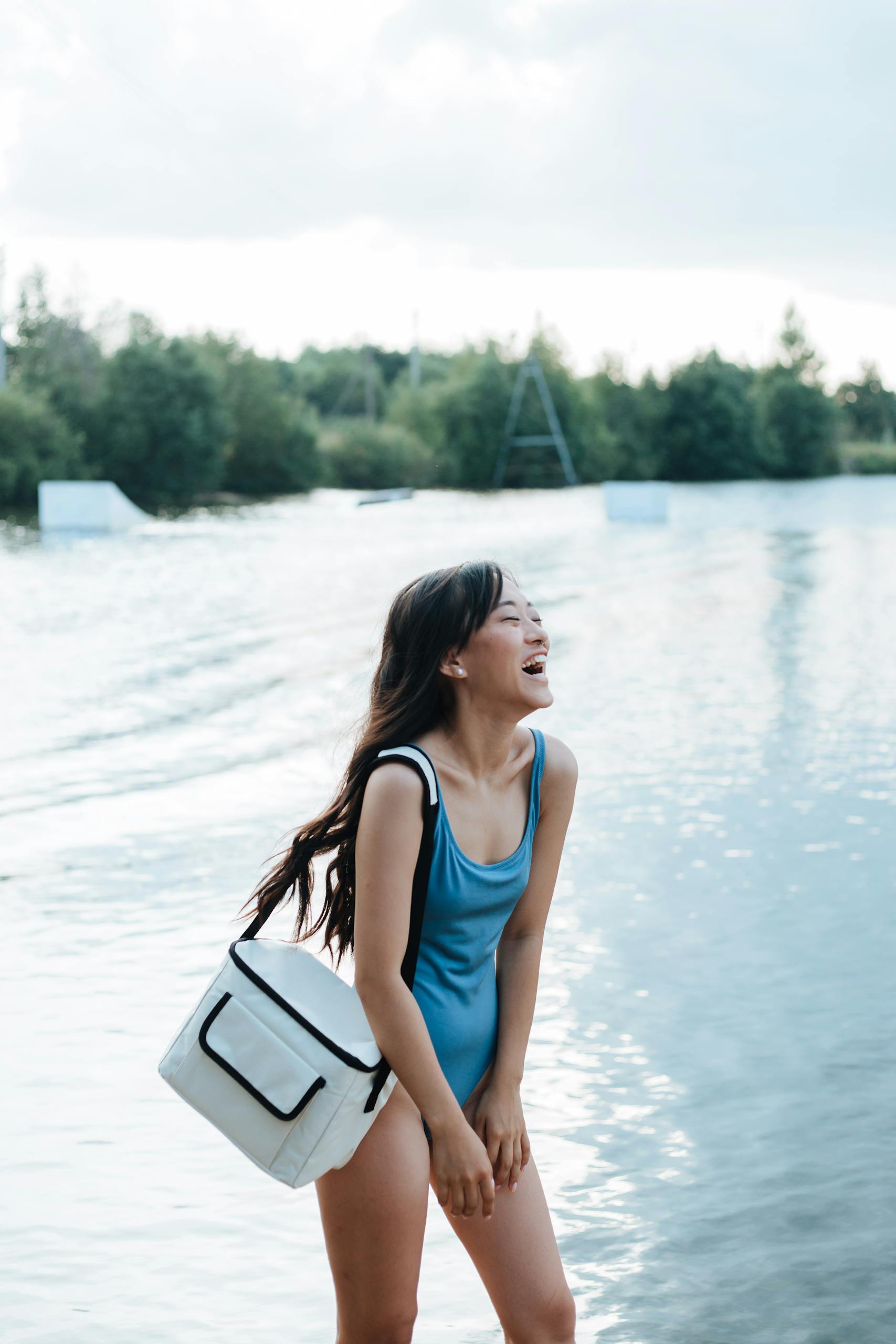 Cheerful woman with long hair laughing by a lake, enjoying a summer day.