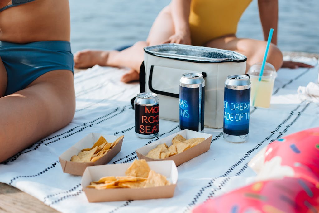 Relaxing summer picnic by the water with snacks, drinks, and swimwear.