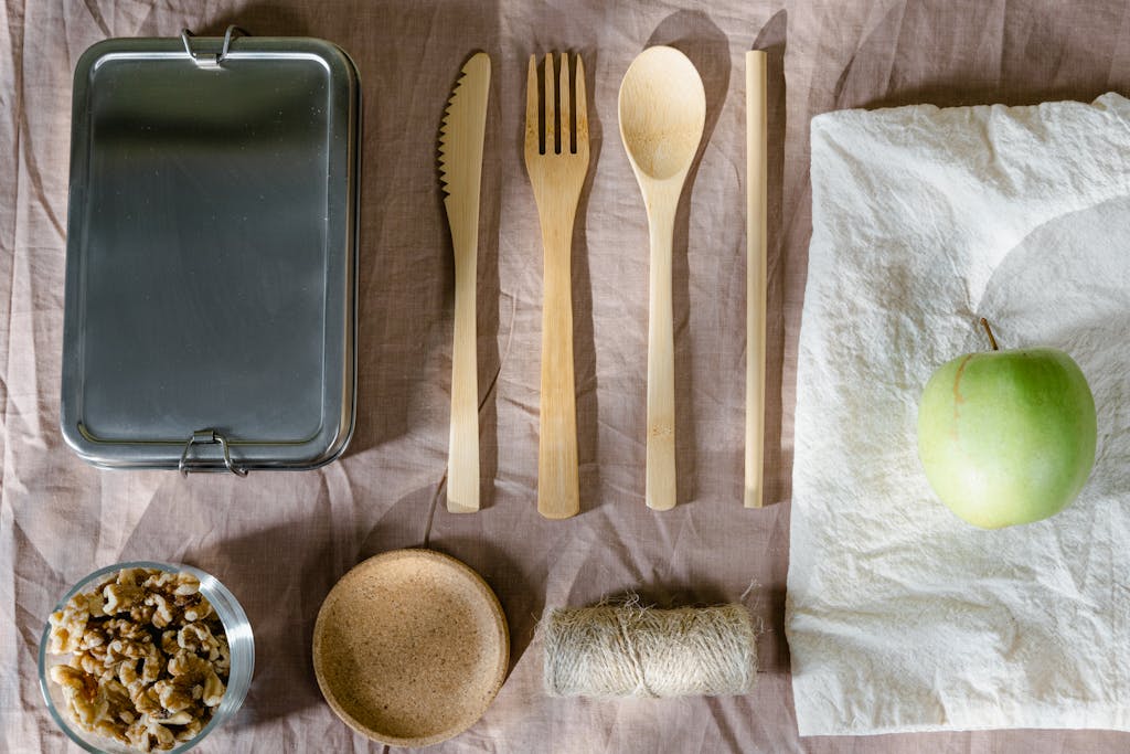 Sustainable flat lay arrangement with wooden utensils, green apple, and lunch box.