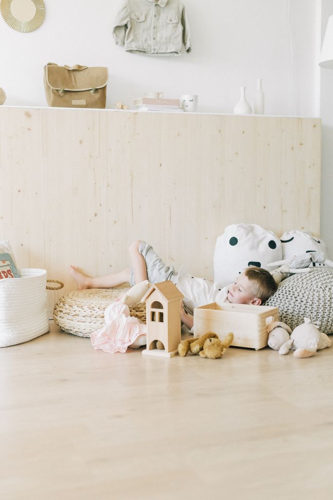 A child resting on cushions in a cozy room, surrounded by plush toys and wooden blocks.