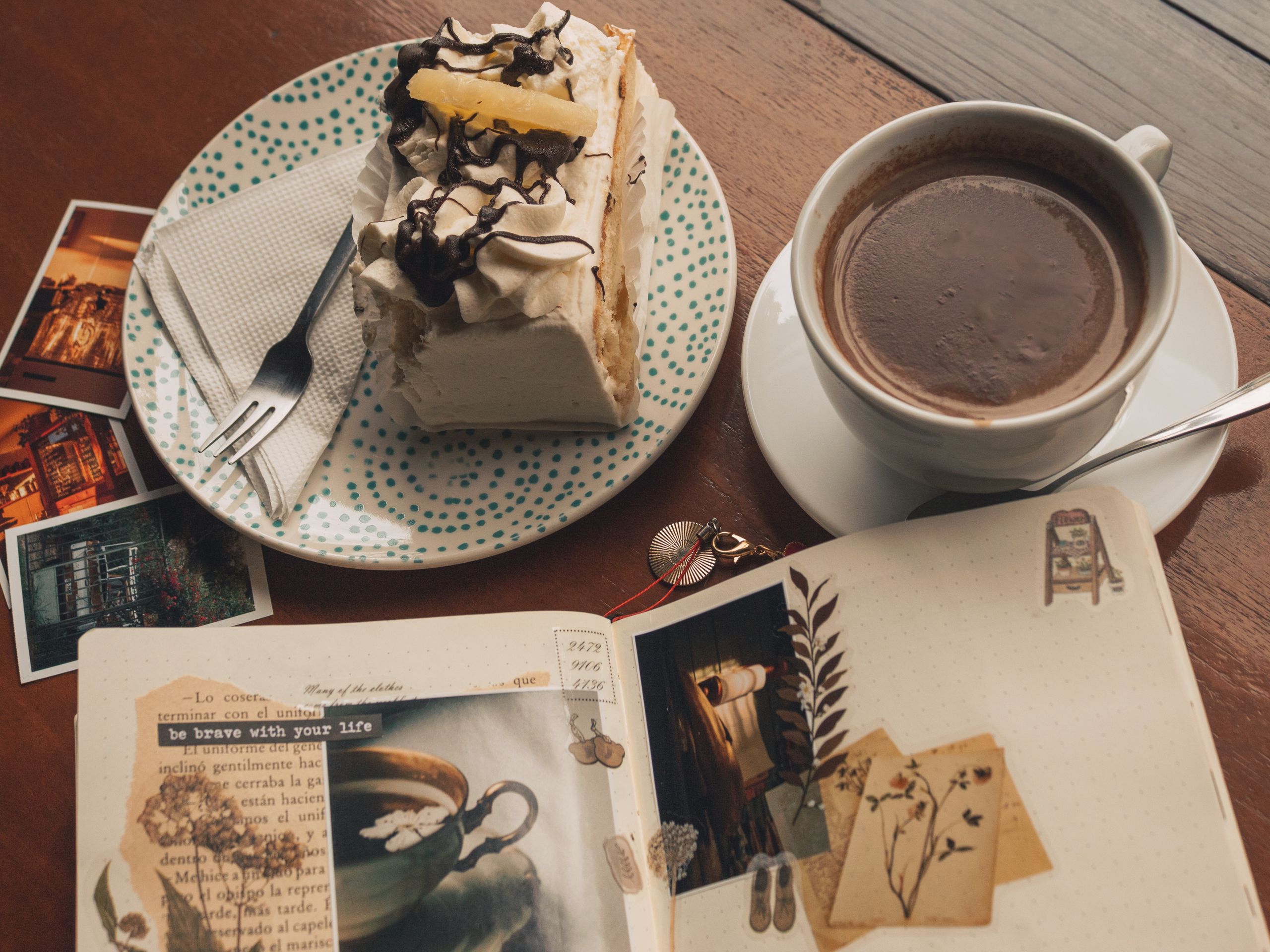 A cozy café setting with a slice of cake, cup of coffee, Polaroids, and an open journal.