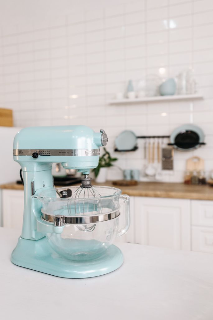 A mint green stand mixer on a kitchen counter with minimalist decor and white tiles.