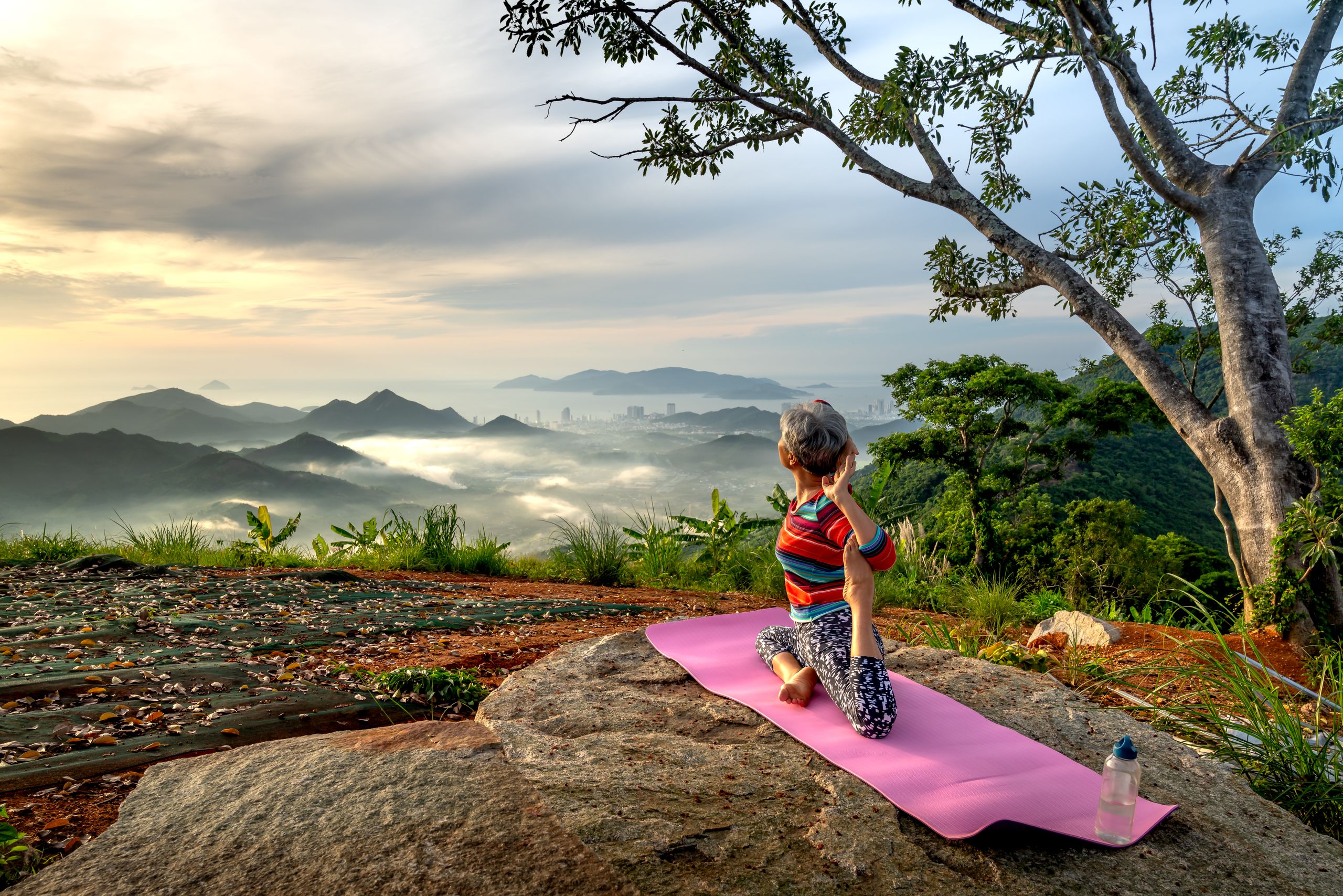 A woman performs yoga on a mountaintop, surrounded by a breathtaking mountain landscape under a serene sky.
