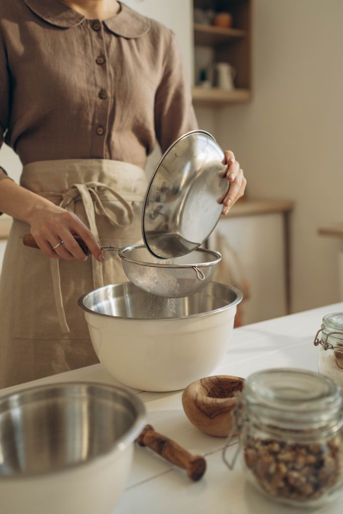 A woman sifts flour into a bowl in a warm, rustic kitchen ambiance, capturing the essence of home baking.