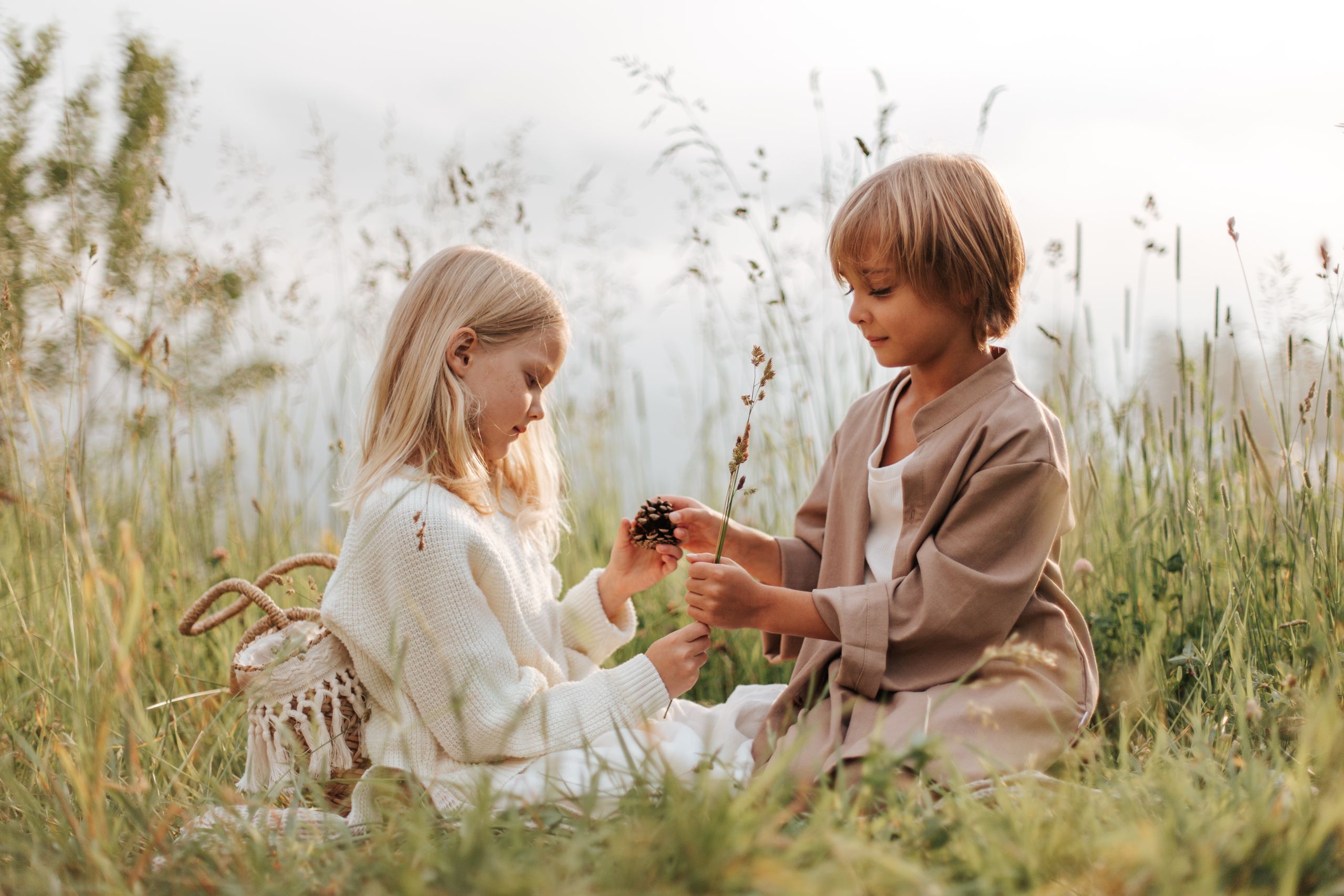Two children sitting and interacting with nature in a grassy field on a sunny day.
