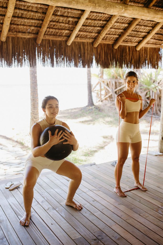 Two women engaged in an outdoor workout, performing functional fitness exercises with equipment.