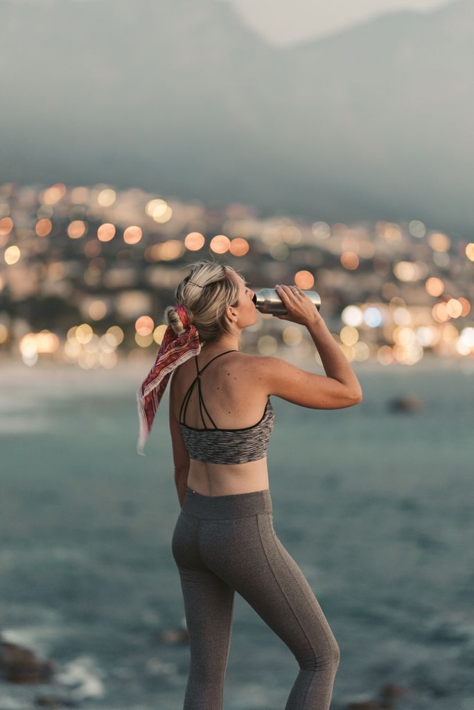 Woman in activewear hydrating while enjoying scenic Cape Town view. Urban bokeh backdrop.