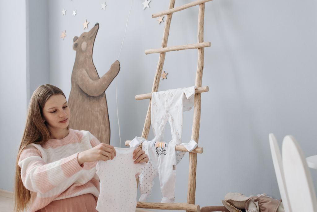 Pregnant woman arranging baby clothes in serene indoor setting with playful decor.