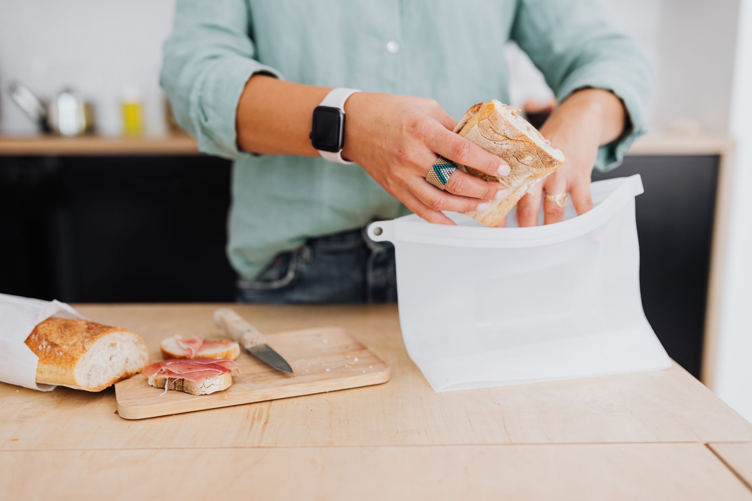 A person packs a sandwich into a silicone bag on a kitchen counter, highlighting eco-friendly food storage.