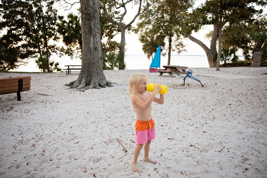 A young child drinks from a non-toxic kids' water bottle on a sandy beach at Hilton Head Island.