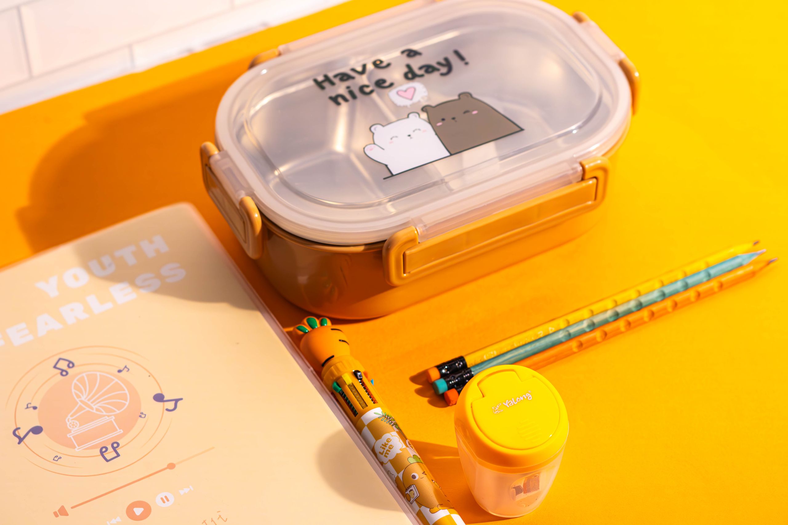 Bright school supplies and lunchbox on a vibrant yellow surface, promoting a cheerful school day.
