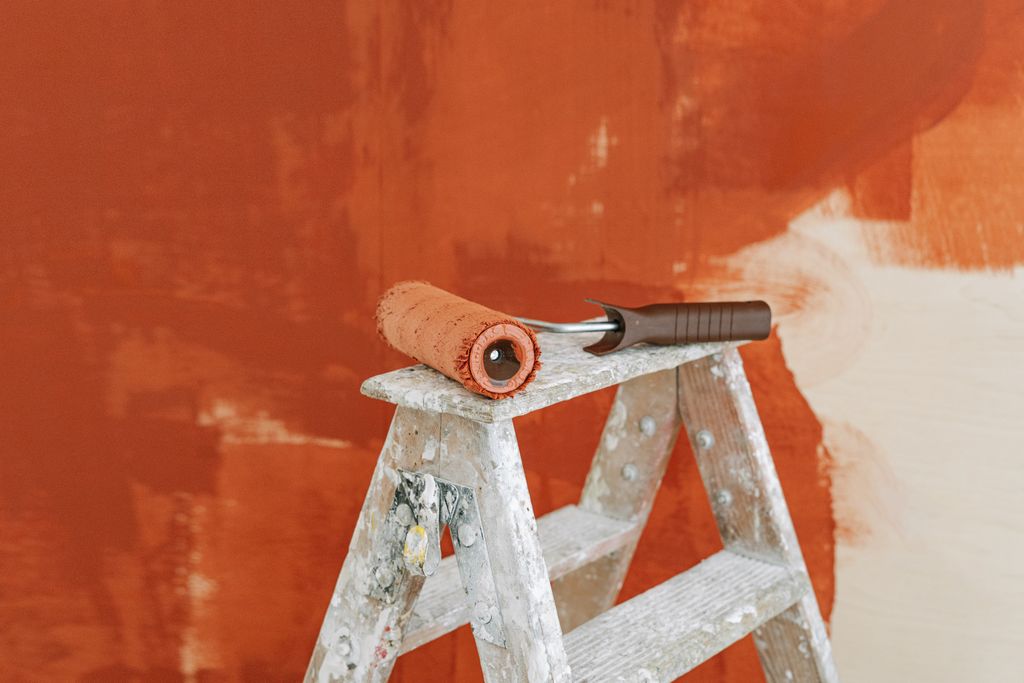 Paint roller on a splattered ladder beside a partially painted red wall, illustrating low-VOC painting for better indoor air
