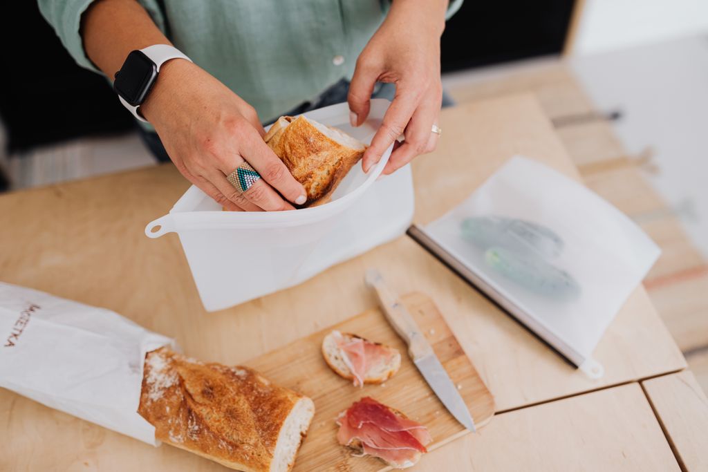 Person packing baguette slices and prosciutto into reusable bags for a plastic free lunch