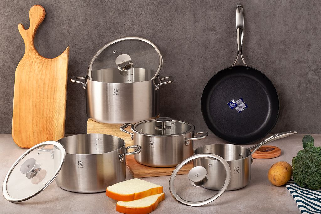 Premium stainless steel cookware set with wooden cutting board, nonstick frying pan and fresh vegetables staged on countertop