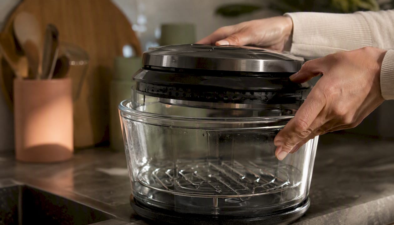 Hands lifting glass air fryer lid revealing interior