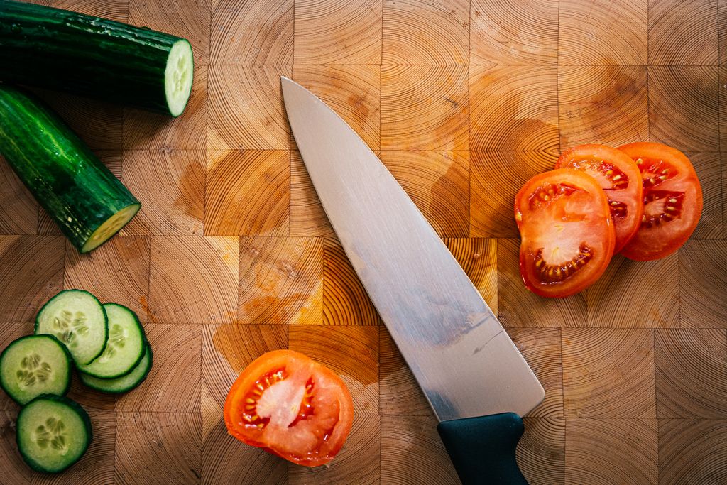 Close-up of hard maple end-grain cutting board with sliced tomatoes, cucumber rounds and a chef’s knife for veggie prep