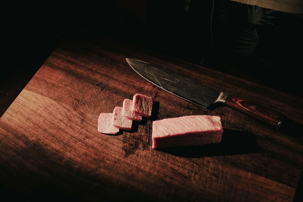 Sliced wagyu beef with exquisite marbling on a wooden board, accompanied by a chef's knife.