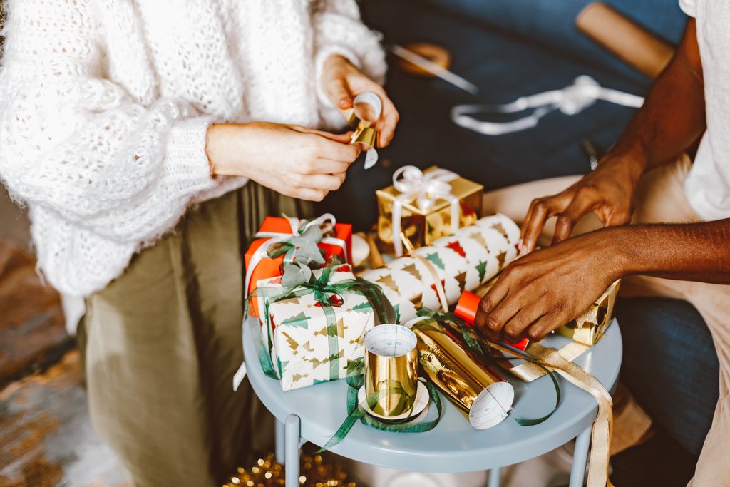 Hands wrapping Christmas gifts with bows and festive wrapping paper indoors.
