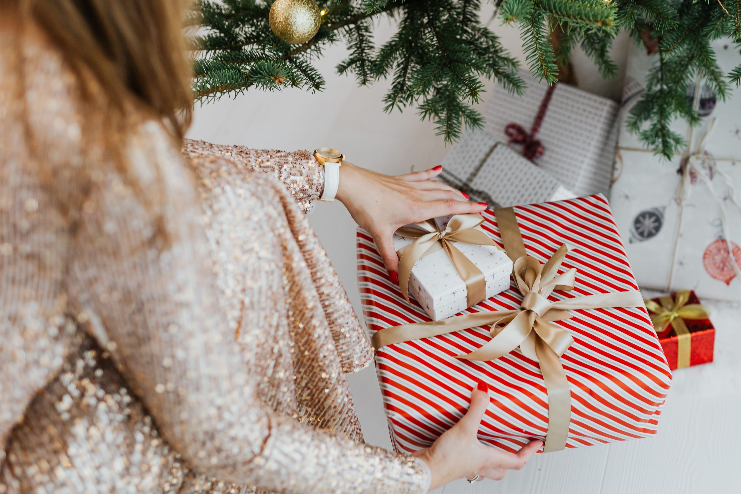 Woman crouching near Christmas tree arranging wrapped gifts at home.
